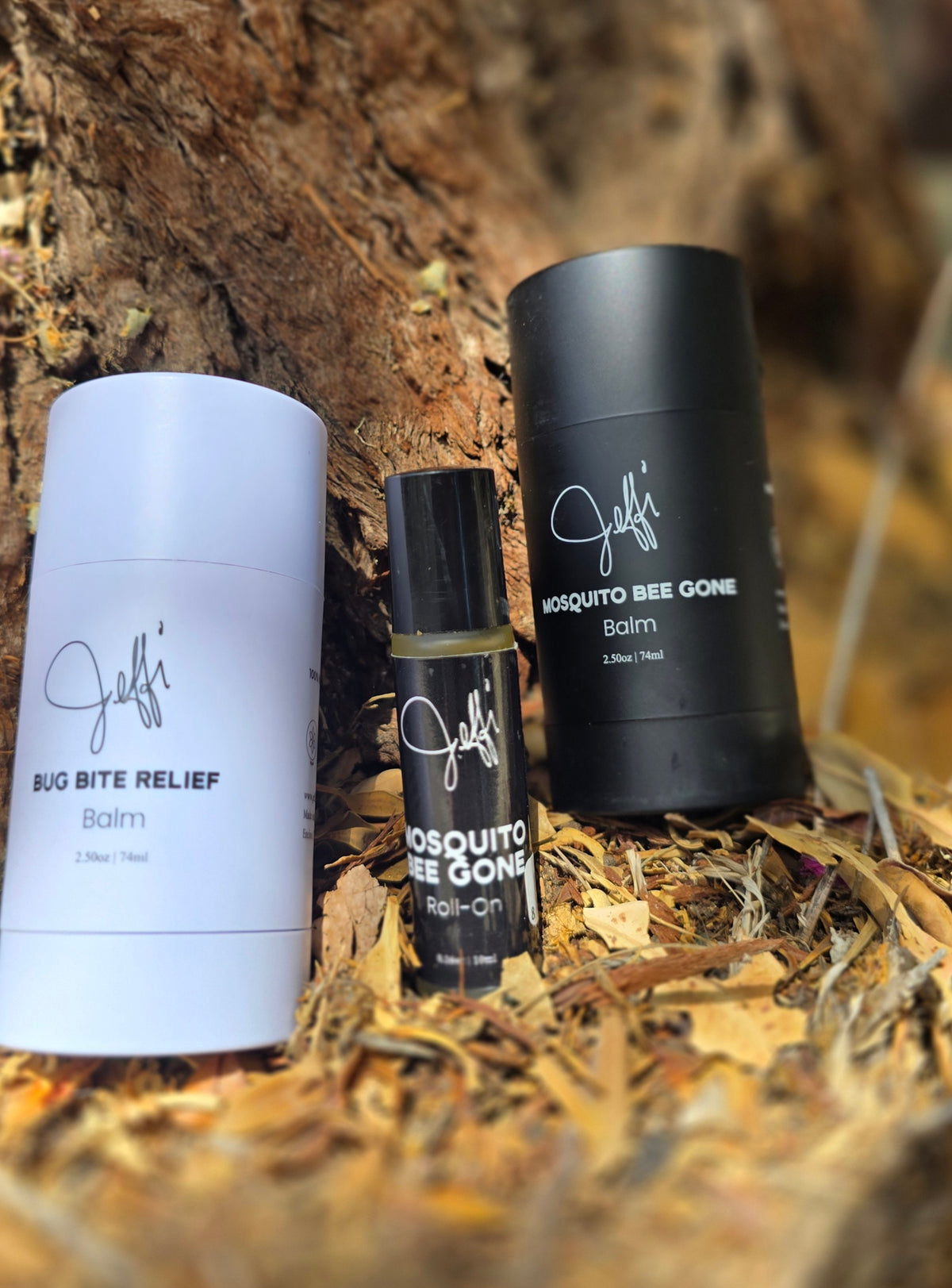 Three personal care products from Jeffi's arranged on a bed of dried leaves and bark: a white tube labeled Bug Bite Relief Balm, a small black roller bottle labeled Mosquito Bee Gone Roll-On, and a black Balm labeled Mosquito Bee Gone Balm.